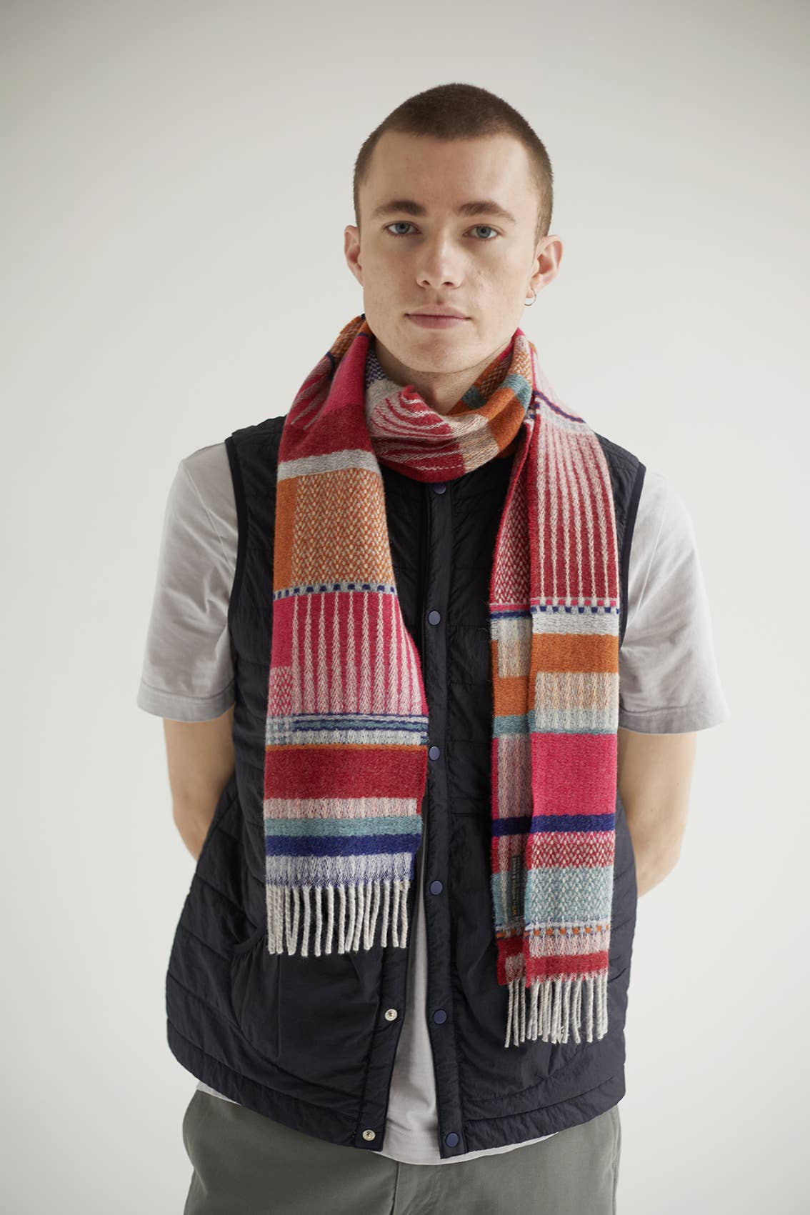 Man wearing a colorful scarf and black vest against a white background