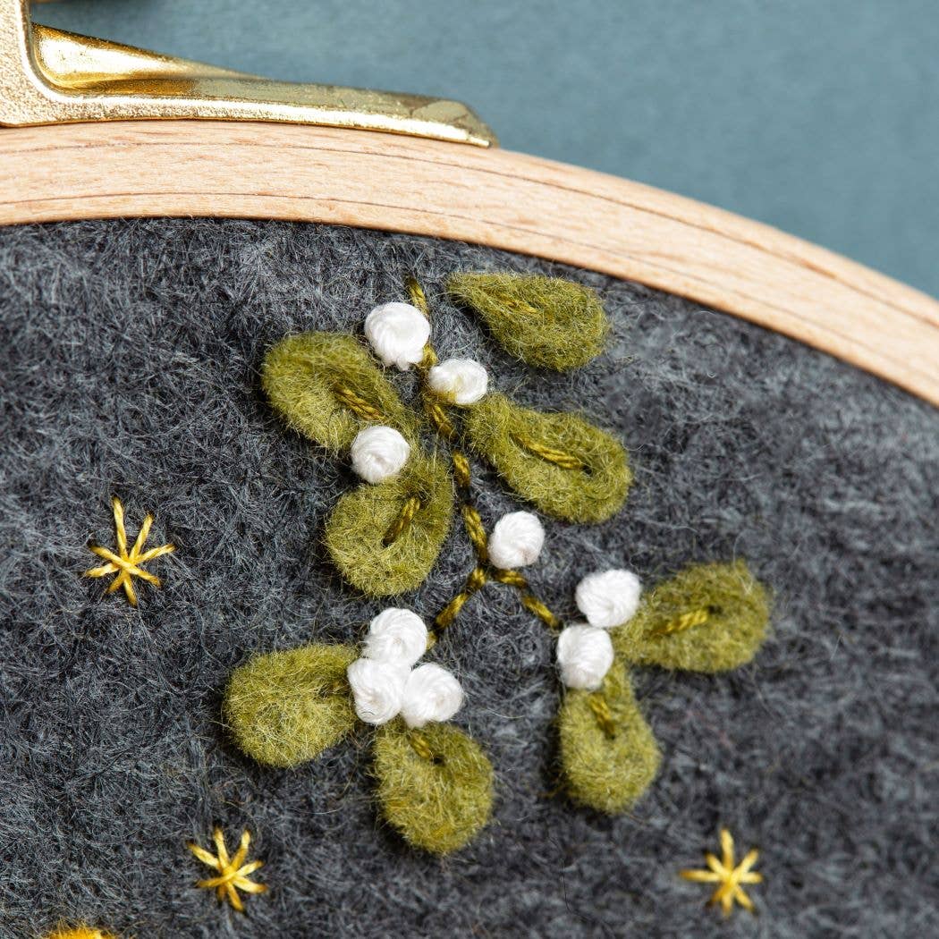 Embroidery hoop with green leaves and white flowers on gray fabric