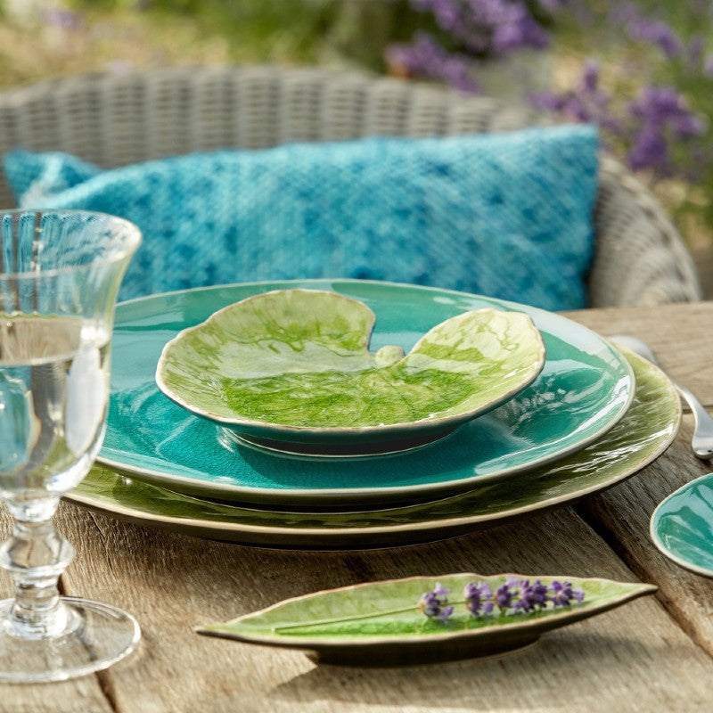 Set of green and turquoise ceramic plates on a wooden table with a blurred background of lavender.