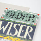 'OLDER WISER' with decorative text and patterns on a white background greetings card