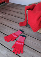 Red gloves with 'Good Day!' text on a wooden surface, accompanied by a red knitted hat.
