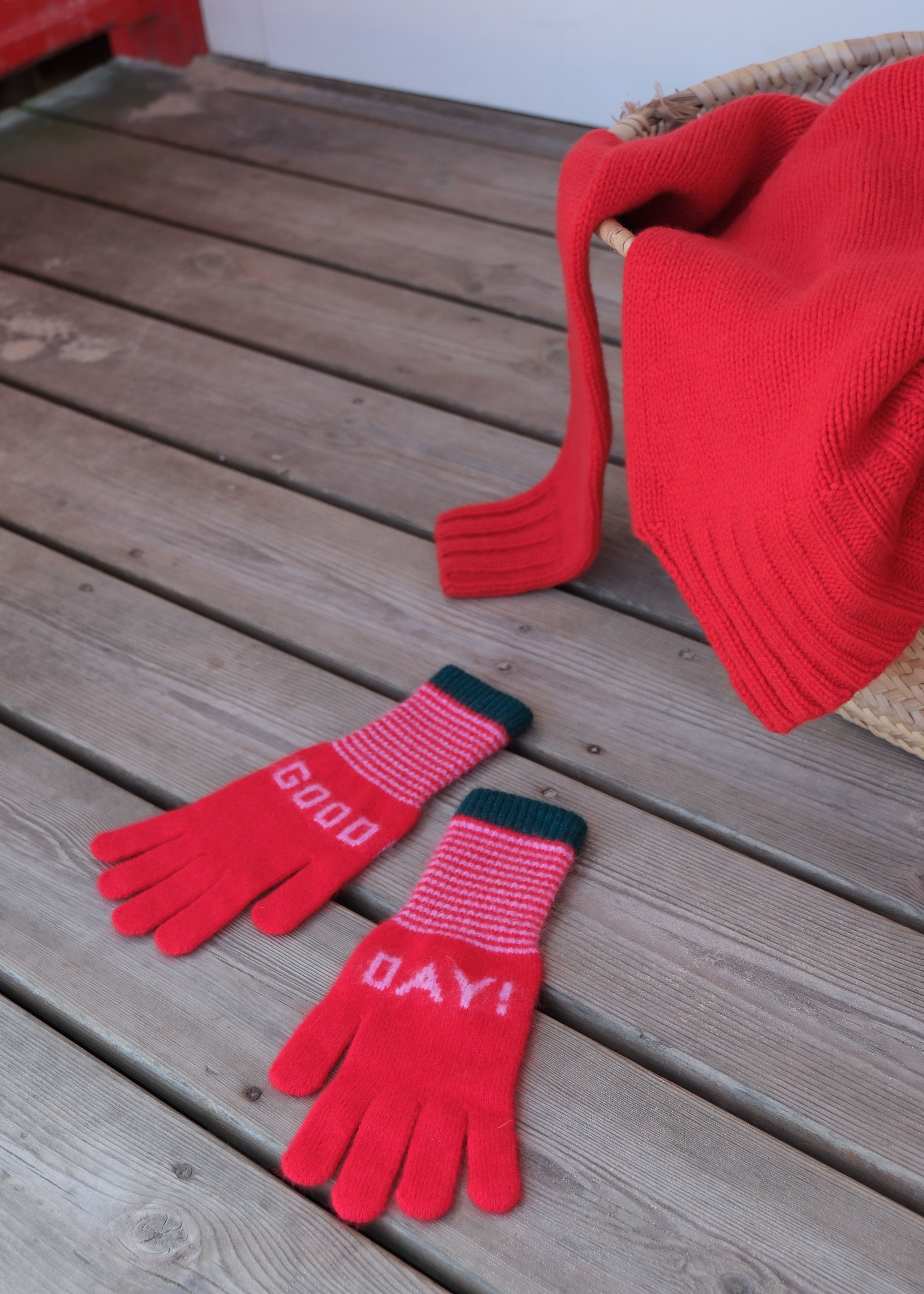 Red gloves with 'Good Day!' text on a wooden surface, accompanied by a red knitted hat.