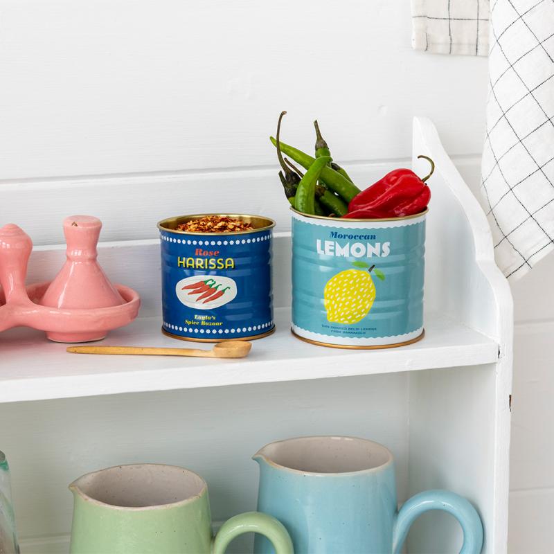 Kitchen shelf with decorative tins labeled 'Harissa' and 'Moroccan Lemons', a pink egg holder, and mugs.