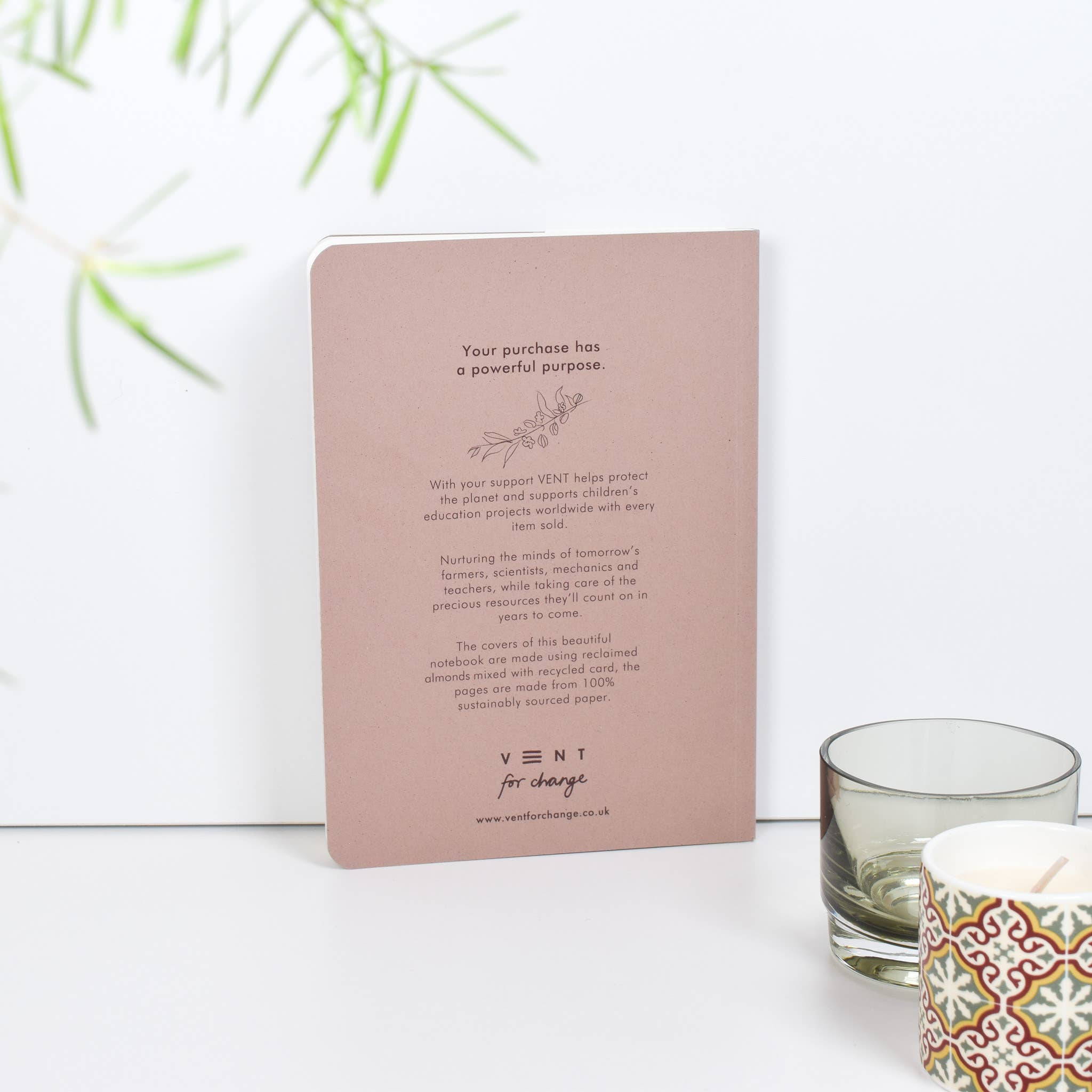 Pink notebook with text on a white surface with a candle and glass in the background