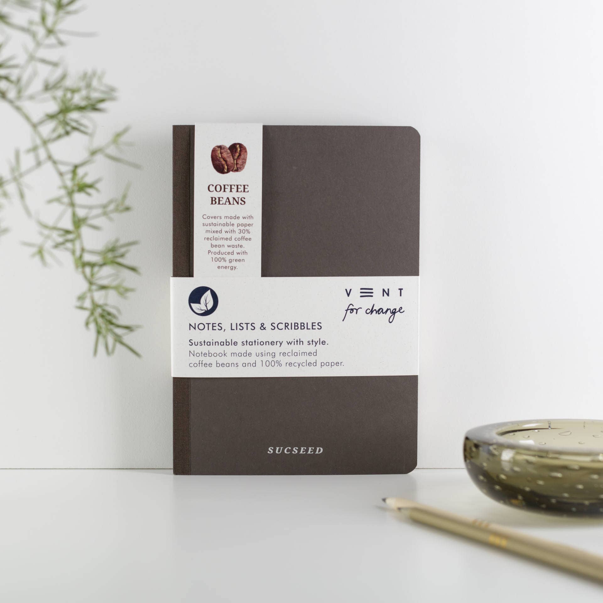 Sustainable notebook with coffee beans and recycled paper on a white surface with a plant in the background