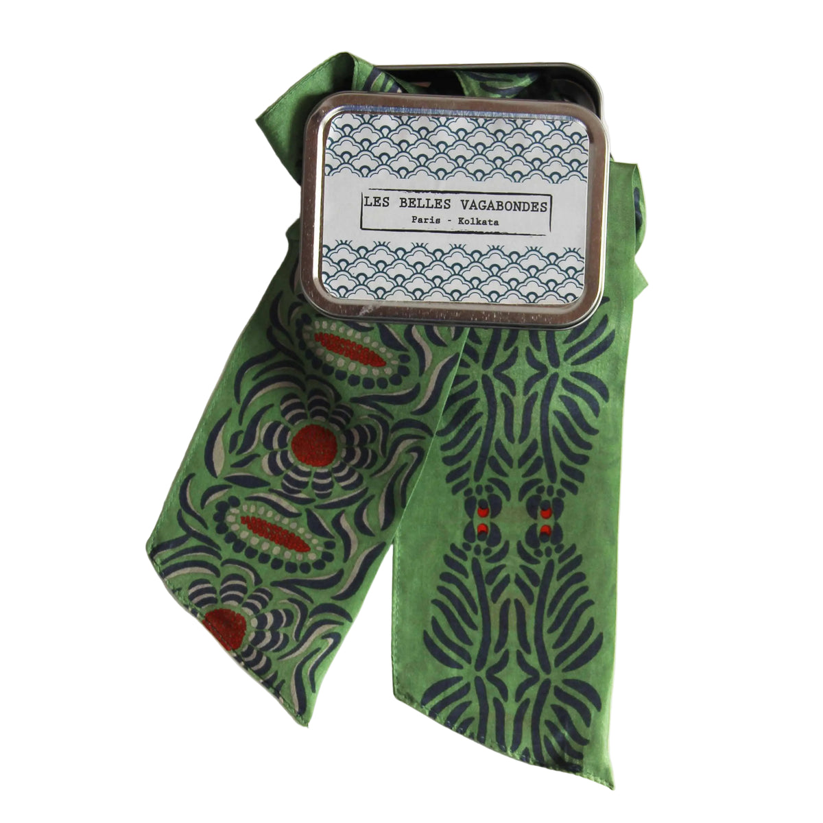 Green patterned ribbon with a small tin labeled 'Les Belles Vagabondes' on a white background