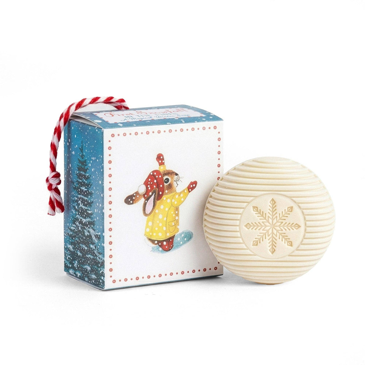 Round soap with snowflake design next to a decorative box featuring a winter-themed illustration on a white background.