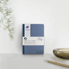 Blue notebook with Lavender Feather branding on a white surface with a plant and candle in the background