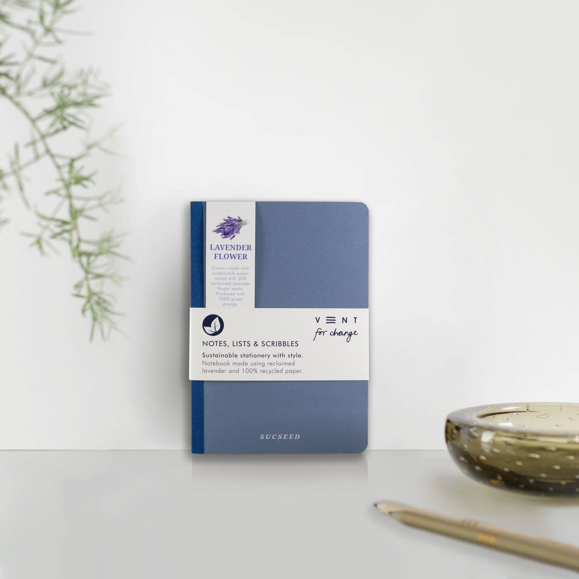 Blue notebook with Lavender Feather branding on a white surface with a plant and candle in the background