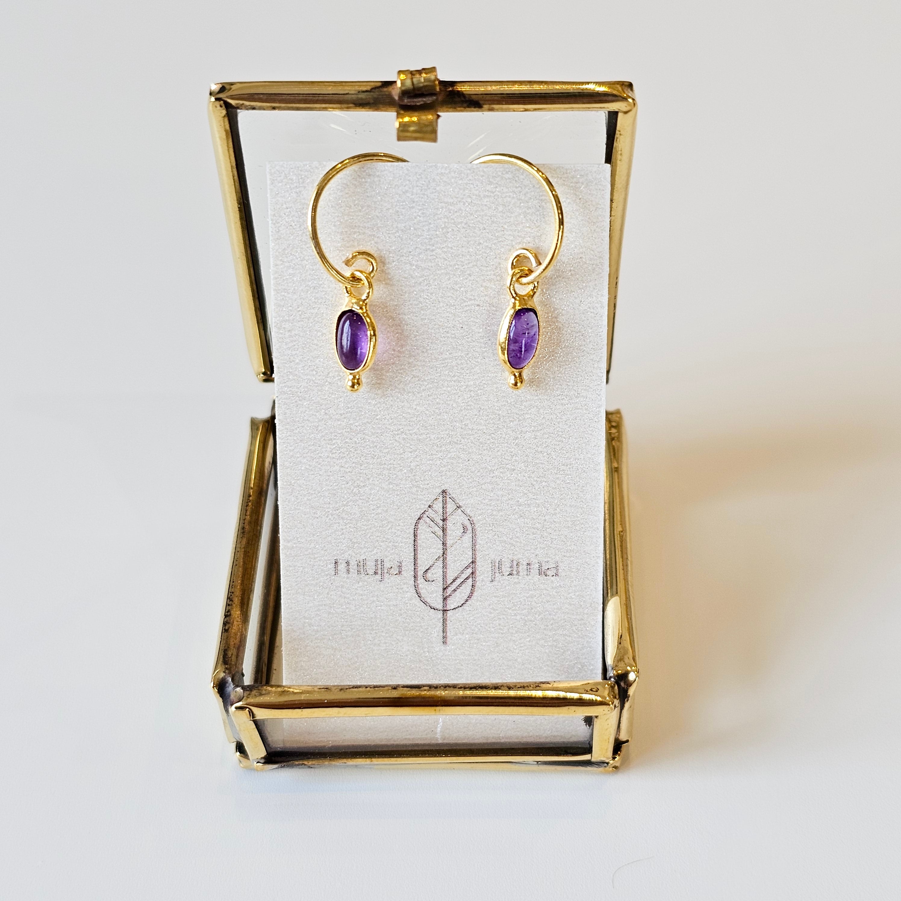 Gold earrings with amethyst stones in a gold display case on a white background