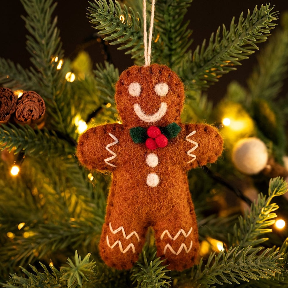 Felt gingerbread man ornament hanging on a Christmas tree with lights in the background