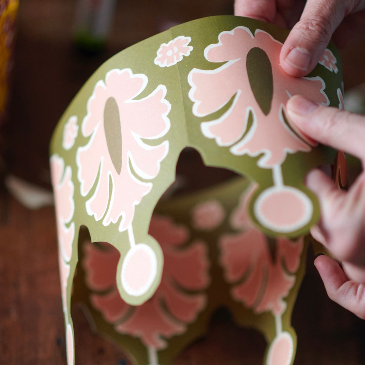 Hand holding a decorative paper cutout with floral patterns on a wooden surface