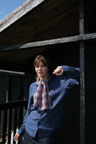 Person wearing a blue shirt and plaid scarf standing on a wooden deck.
