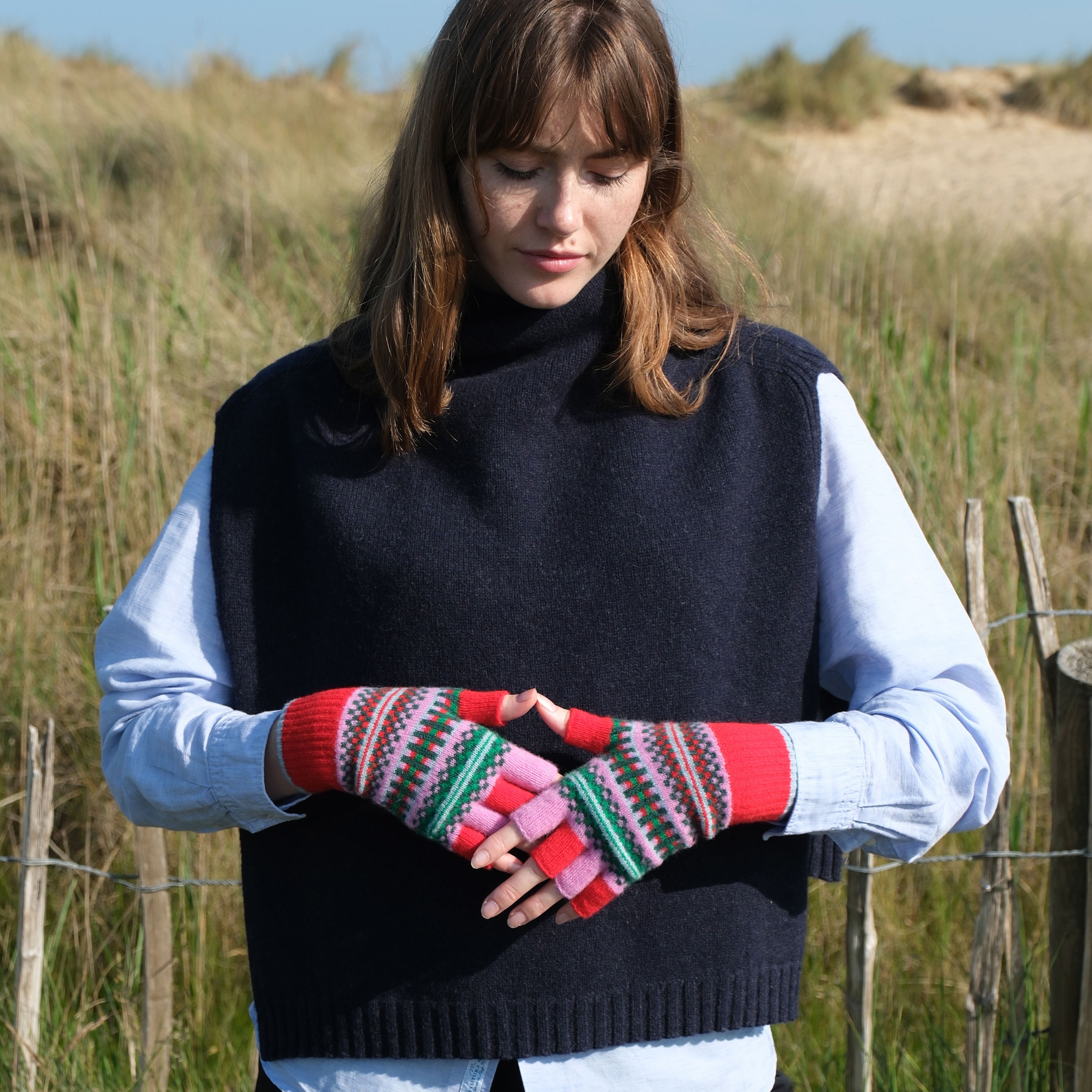 Woman wearing a black sleeveless sweater and colorful fingerless gloves in a field.