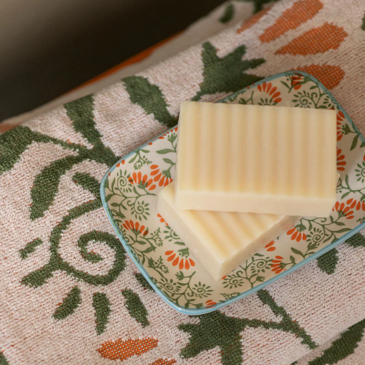 Two bars of soap on a decorative soap dish on a patterned towel