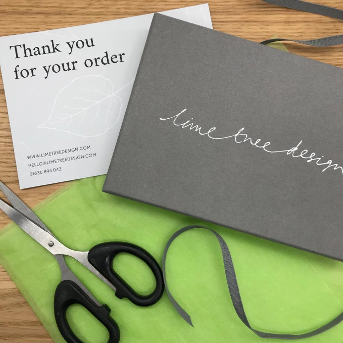 Grey box with 'lime tree design' branding, scissors, and green fabric on a wooden surface.