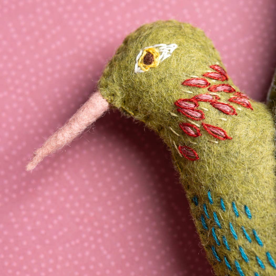 Close-up of a green embroidered hummingbird decoration on a pink polka dot background