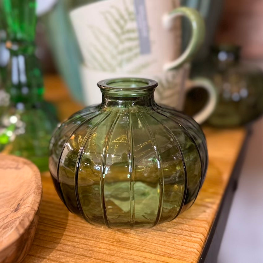 Green ribbed glass vase on a wooden surface with blurred background
