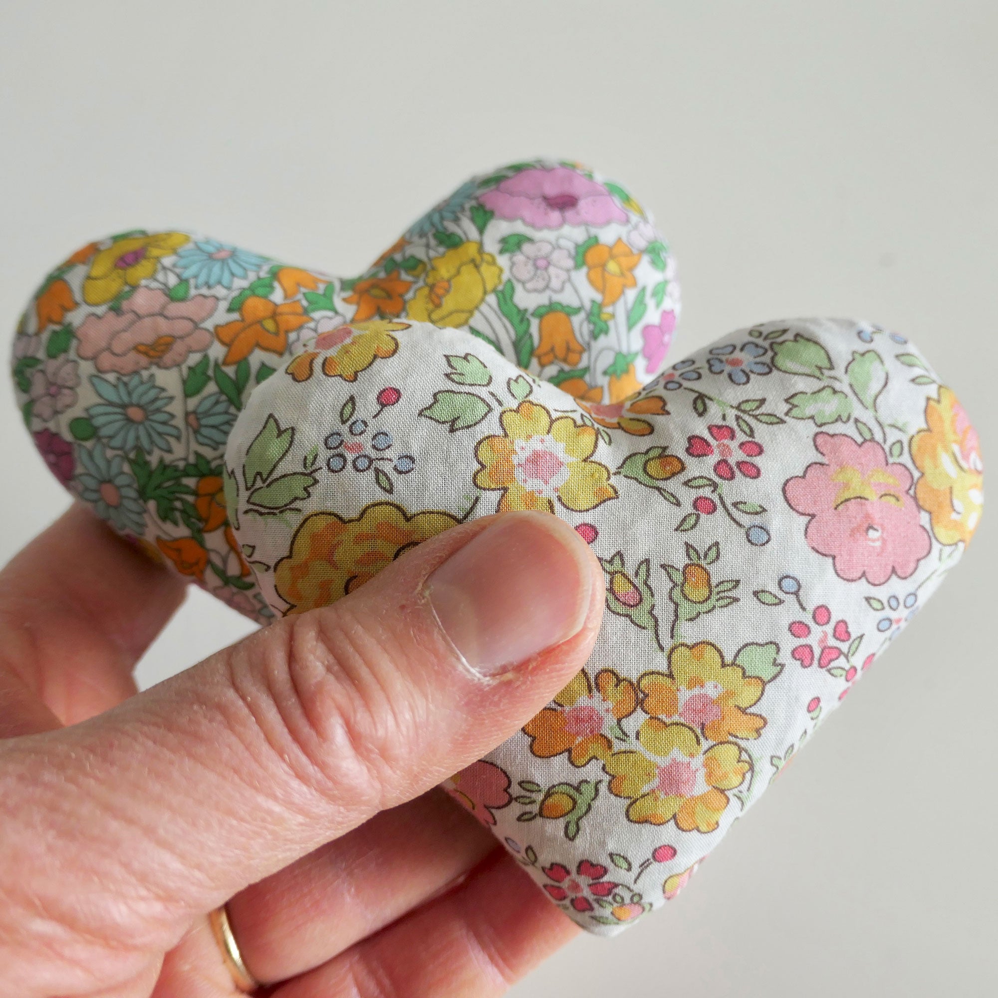 Hand holding a floral-patterned heart-shaped fabric item against a plain background