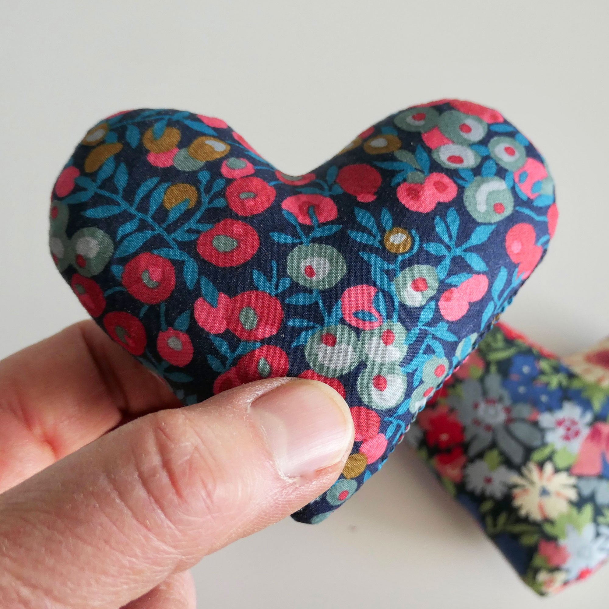 Hand holding a floral-patterned heart-shaped fabric item against a white background