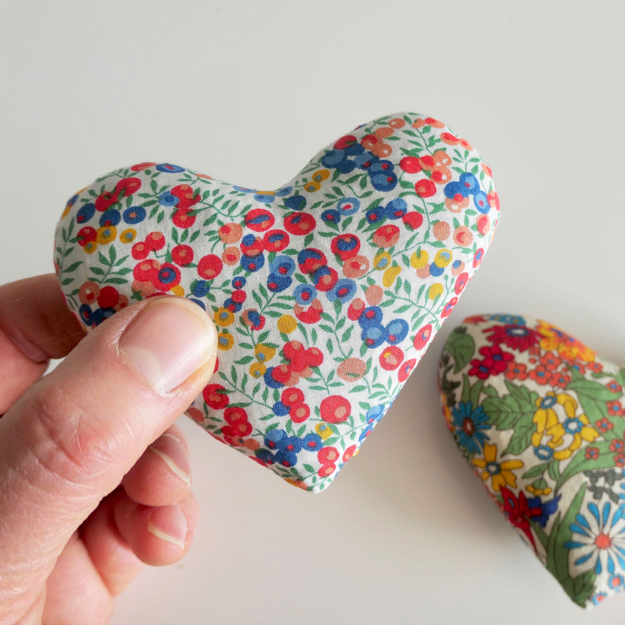 Hand holding a floral-patterned heart-shaped fabric item on a light background