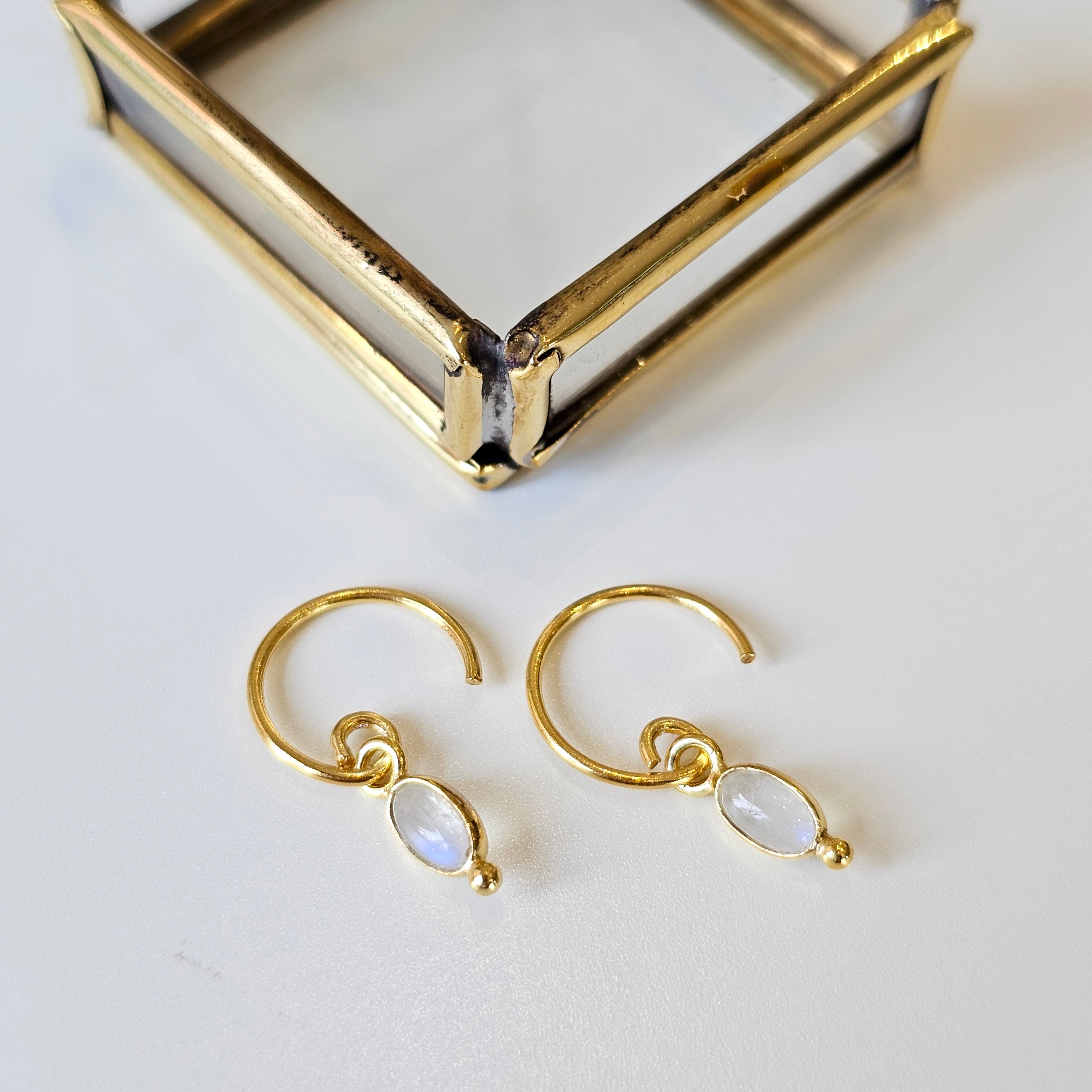 Gold hoop earrings with moonstone drops on a white surface