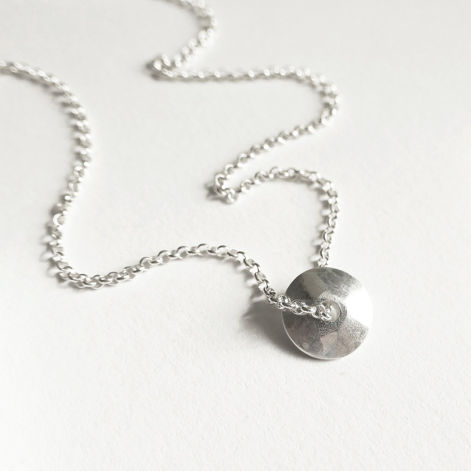 Silver necklace with a heart-shaped pendant on a white background