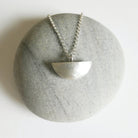 Silver necklace with a half-circle pendant on a textured stone surface