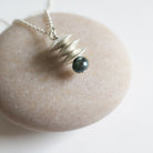 Silver necklace with a dark bead pendant on a light stone surface