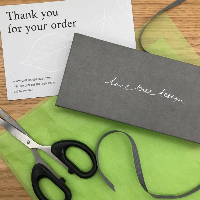 Grey box with 'lime tree design' branding, scissors, and green paper on a wooden surface.
