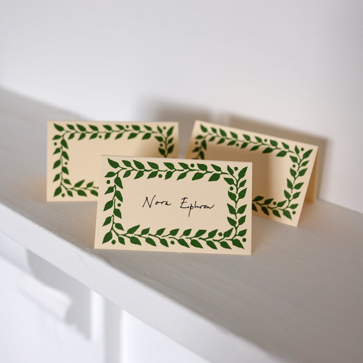 Three beige cards with green leaf patterns on a white surface