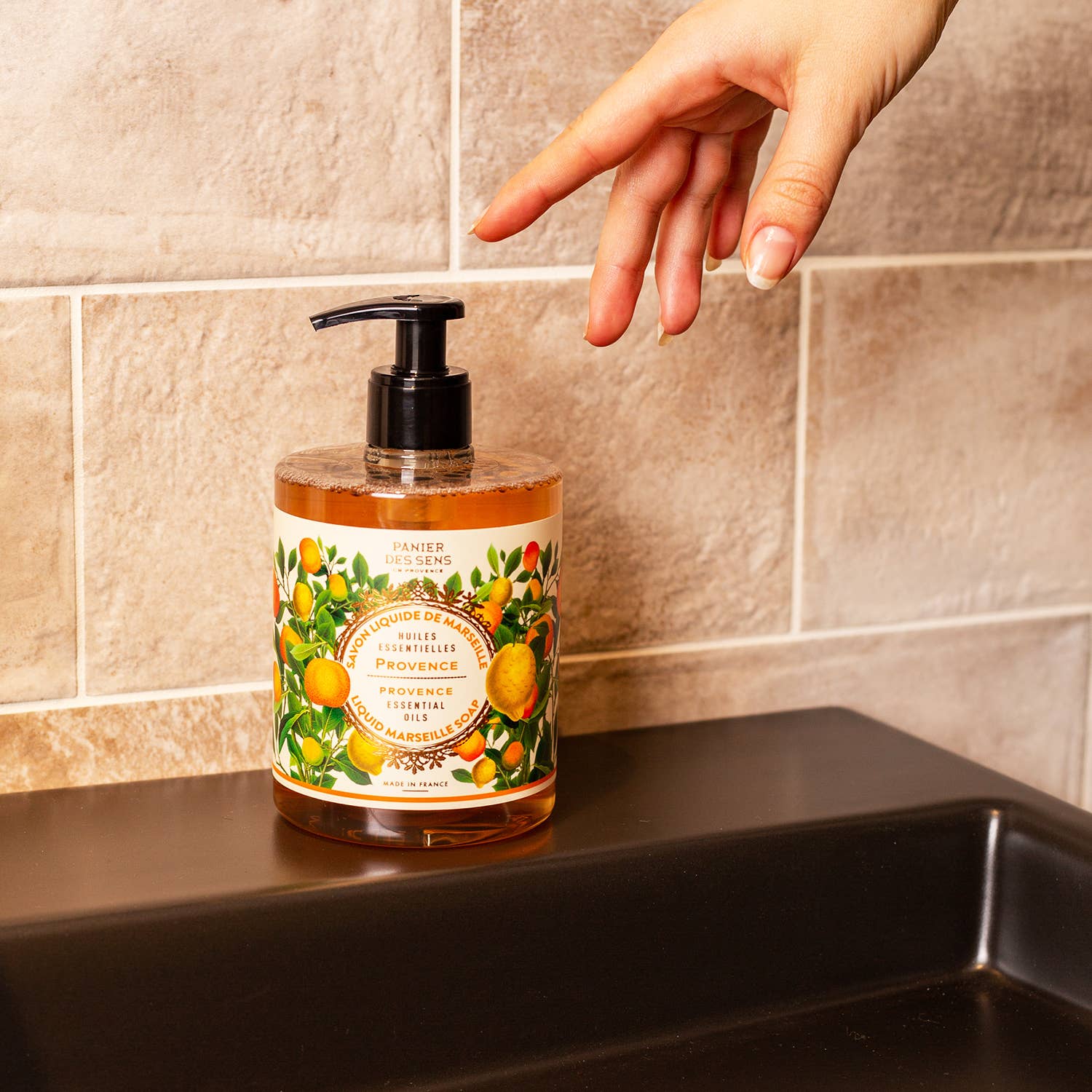 Hand soap bottle with decorative label on a sink, hand reaching to pump it.