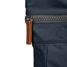 Close-up of a navy blue bag with a brown zipper pull on a white background