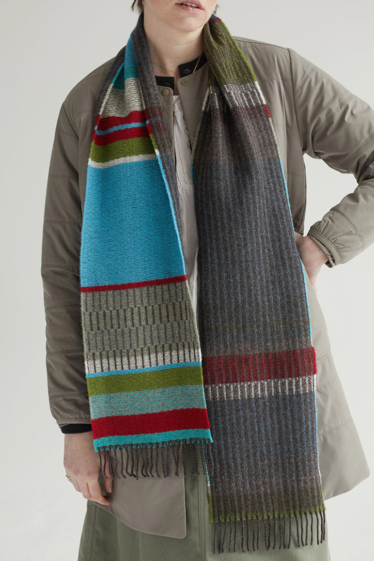 Person wearing two scarves, one with colorful stripes and the other gray, on a plain background.