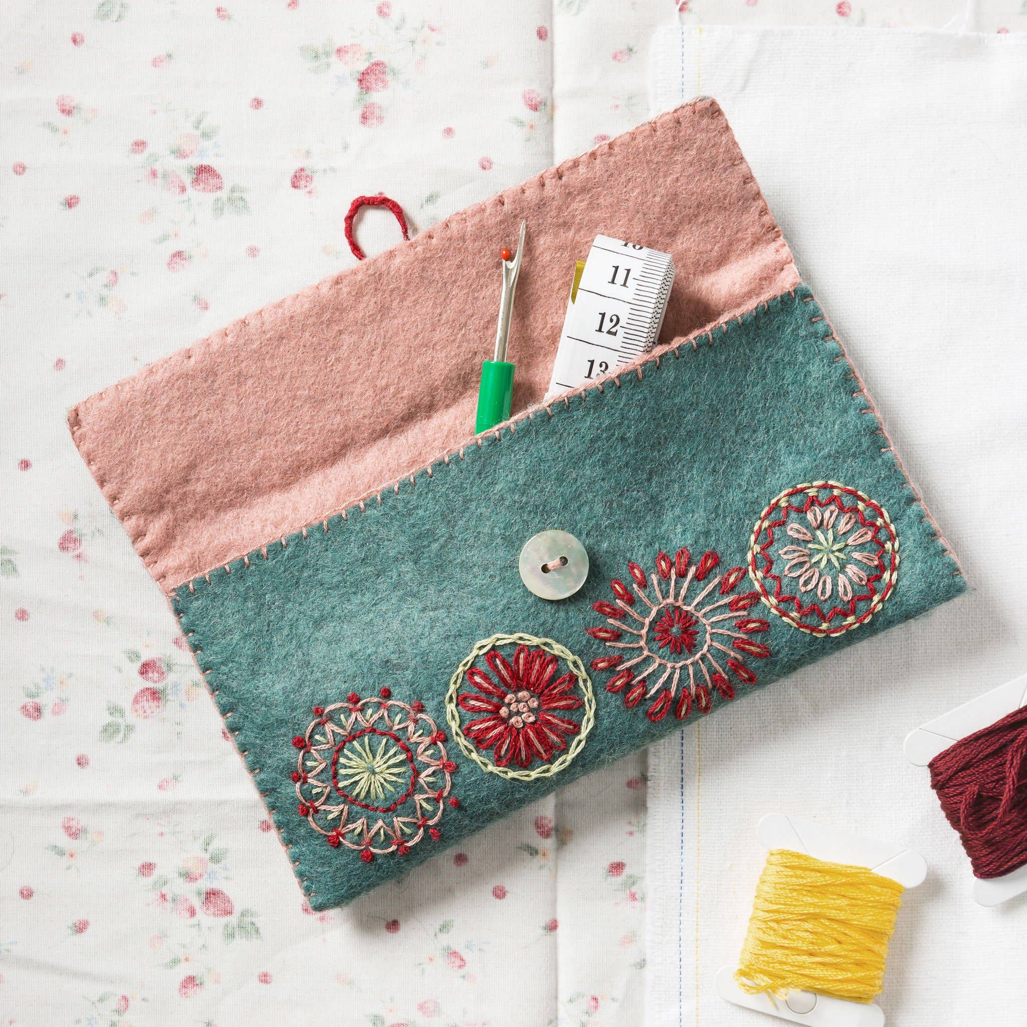 Sewing pouch shown open with sewing paraphernalia stored inside and laid around it.