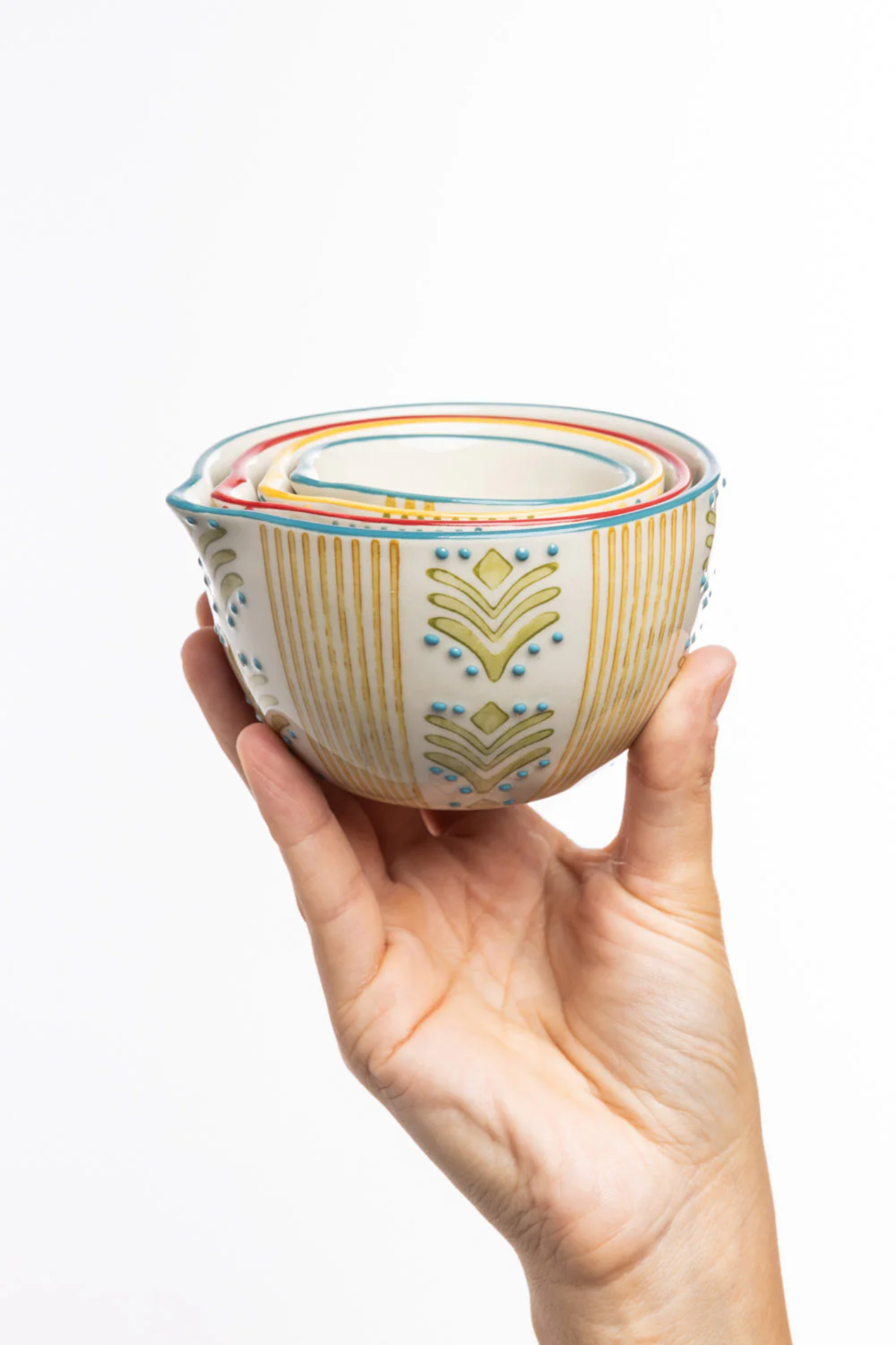 Hand holding a set of stacked ceramic jugs with decorative patterns on a white background