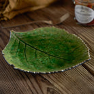 Green leaf-shaped ceramic plate on a wooden surface with a blurred jar in the background.