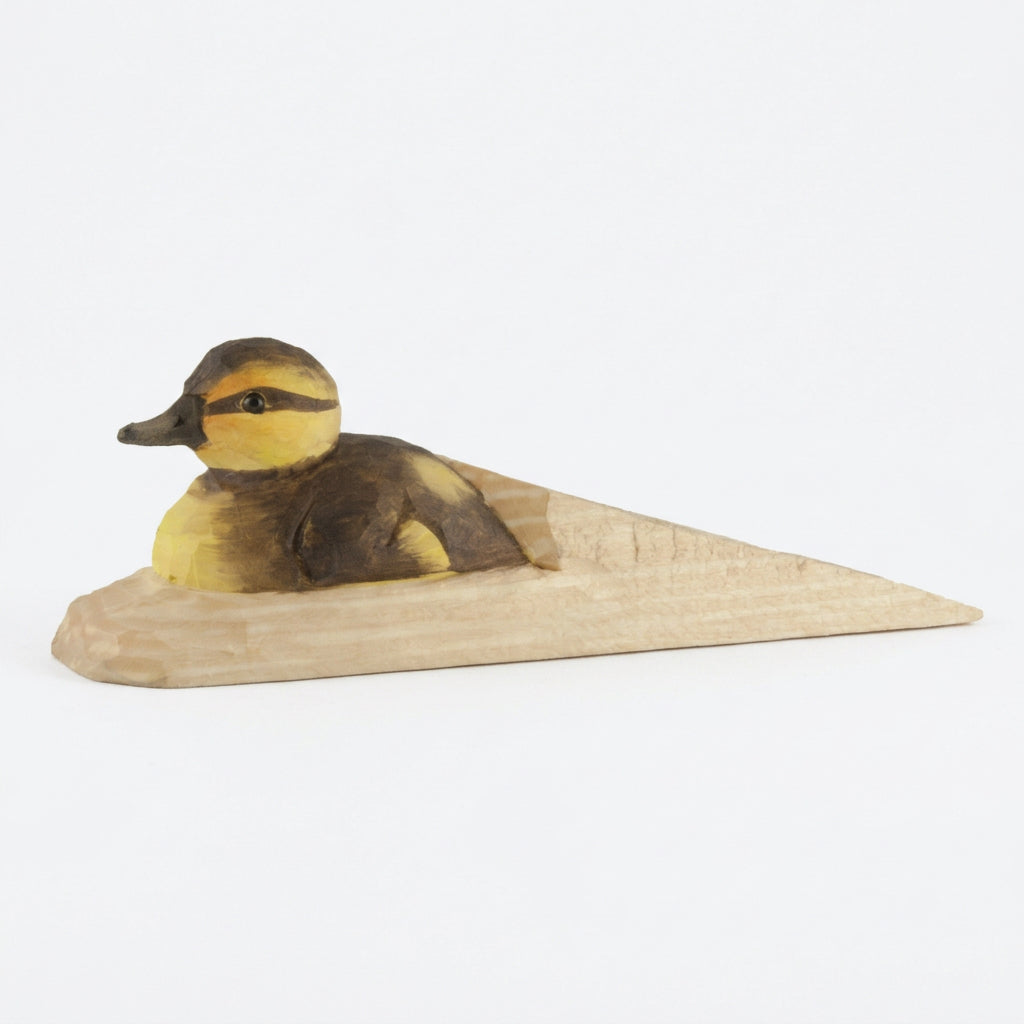 A handcrafted wooden duck figurine with a yellow and brown painted body, mounted on a triangular light wood base against a plain white background.