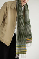 Person wearing a patterned scarf with a beige jacket on a white background