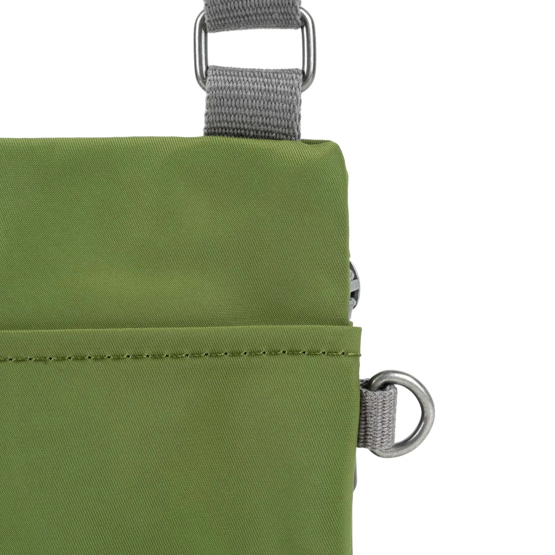 A close up photo of the back of a avocado green bag, showing the grey strap and neatly stitched pocket opening.