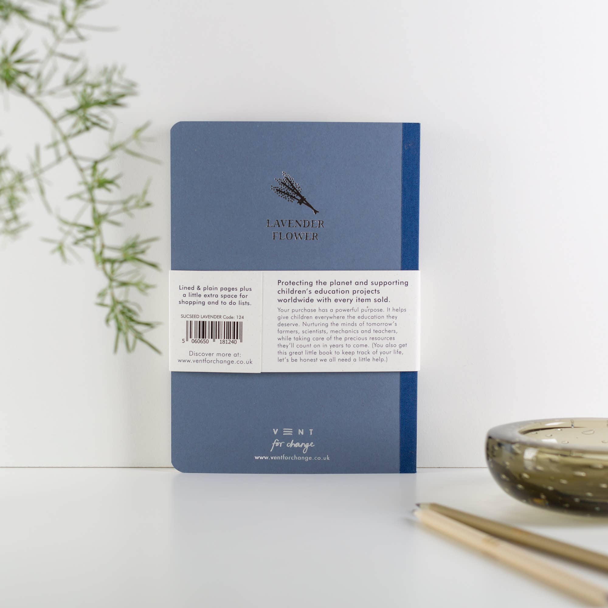 Blue notebook with branding on a white surface with a plant and candle in the background