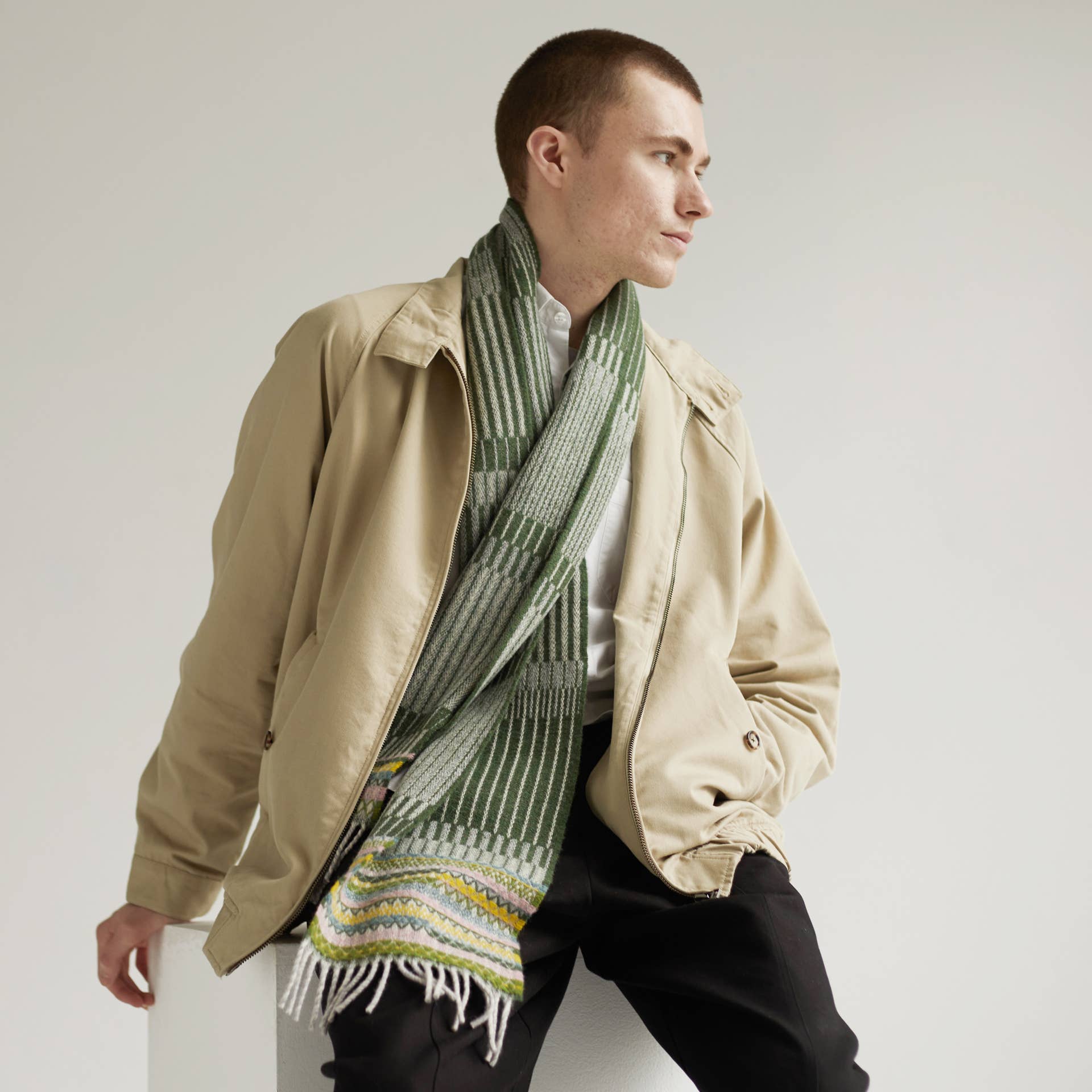 Man wearing a beige jacket and green scarf against a plain background