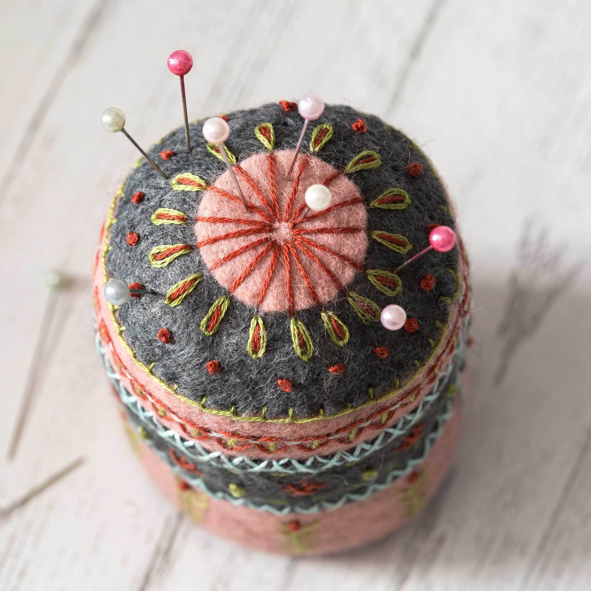Embroidered pincushion with pins on a light wooden surface