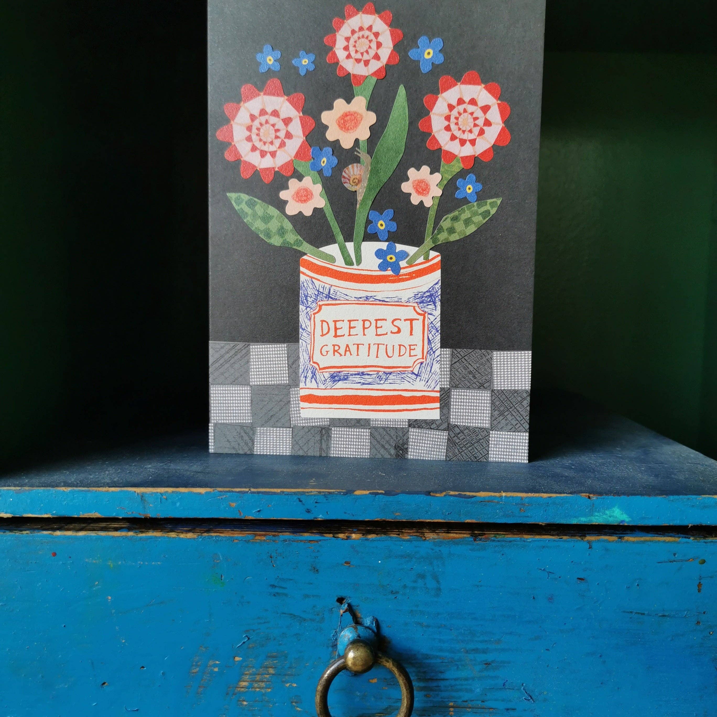 Greeting card with floral design and 'Deepest Gratitude' text on a blue wooden surface.