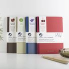 Four notebooks with different colored covers and labels on a white surface.