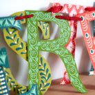 Colorful paper letters 'R' and 'S' with decorative patterns on a wooden surface.