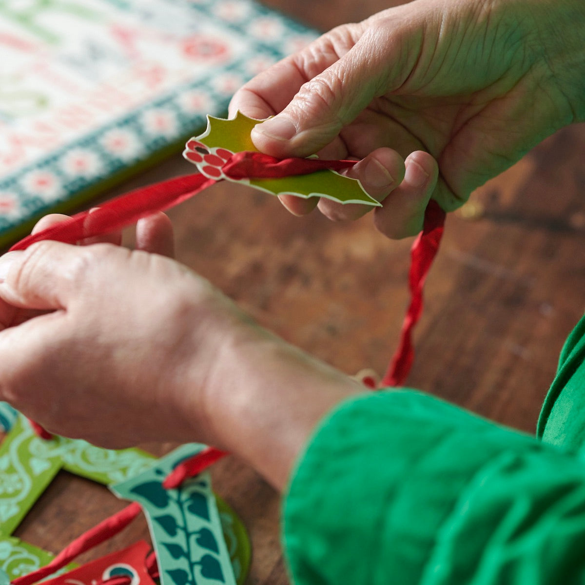 Close-up of hands tying a red ribbon on a green leaf-shaped object.