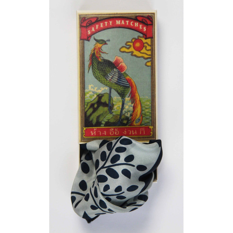 Vintage safety matches box with a colorful design featuring a bird, next to a black and white patterned scarf on a white background.
