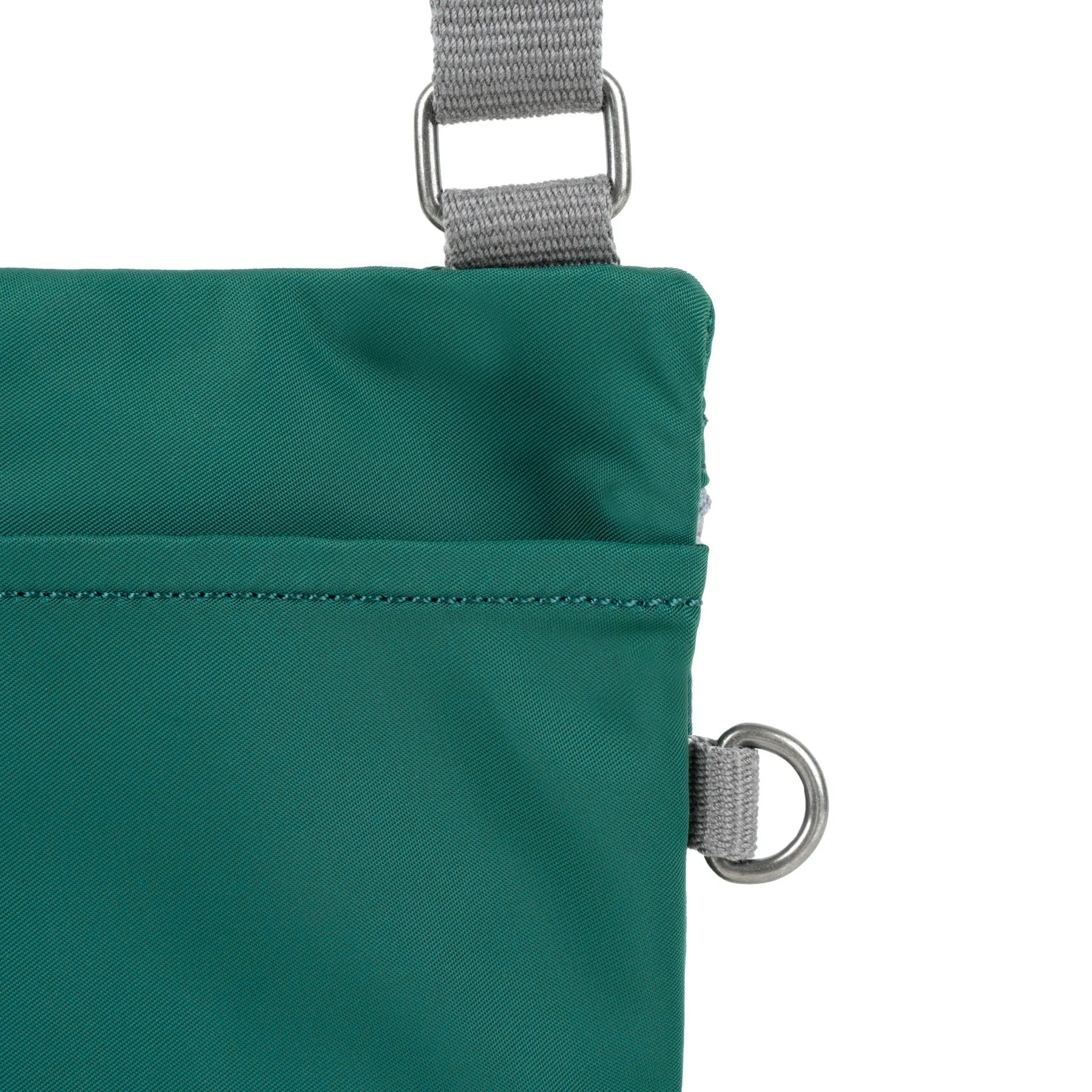 A close up photo of the back of a teal bag, showing the grey strap and neatly stitched pocket opening.