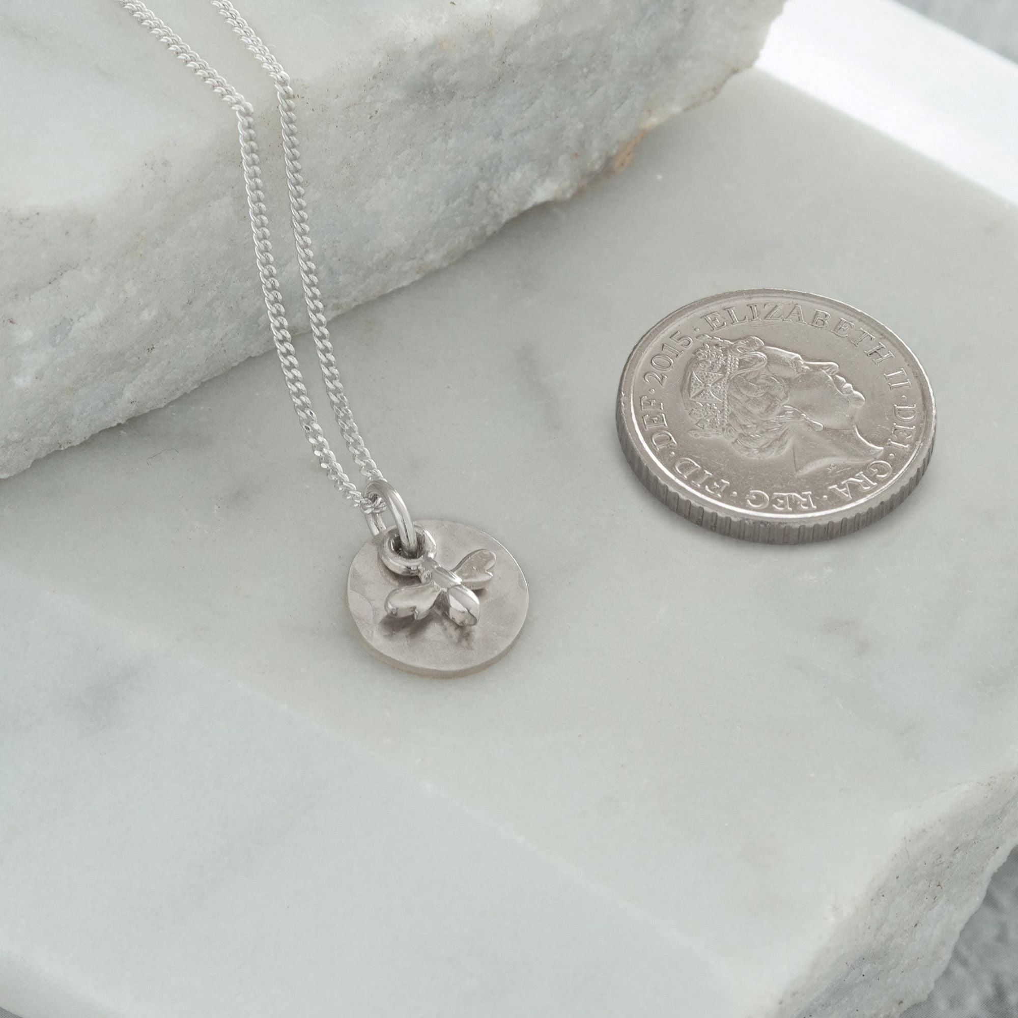 mini bee necklace next to coin for size